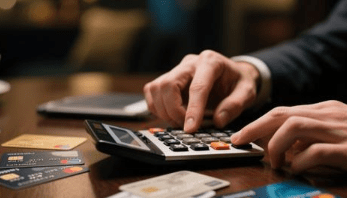 Close-up of hands using a calculator with multiple credit cards on the table.
